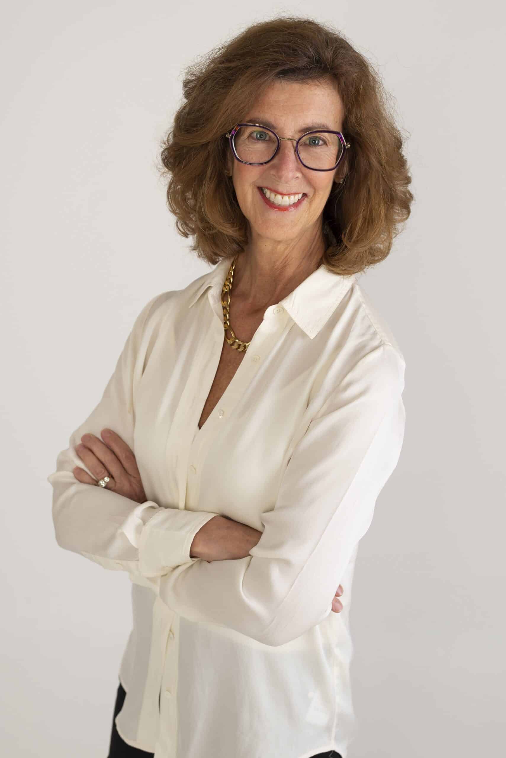 Image of Nancy Clairmont Carr standing with arms crossed in a white button down shirt.